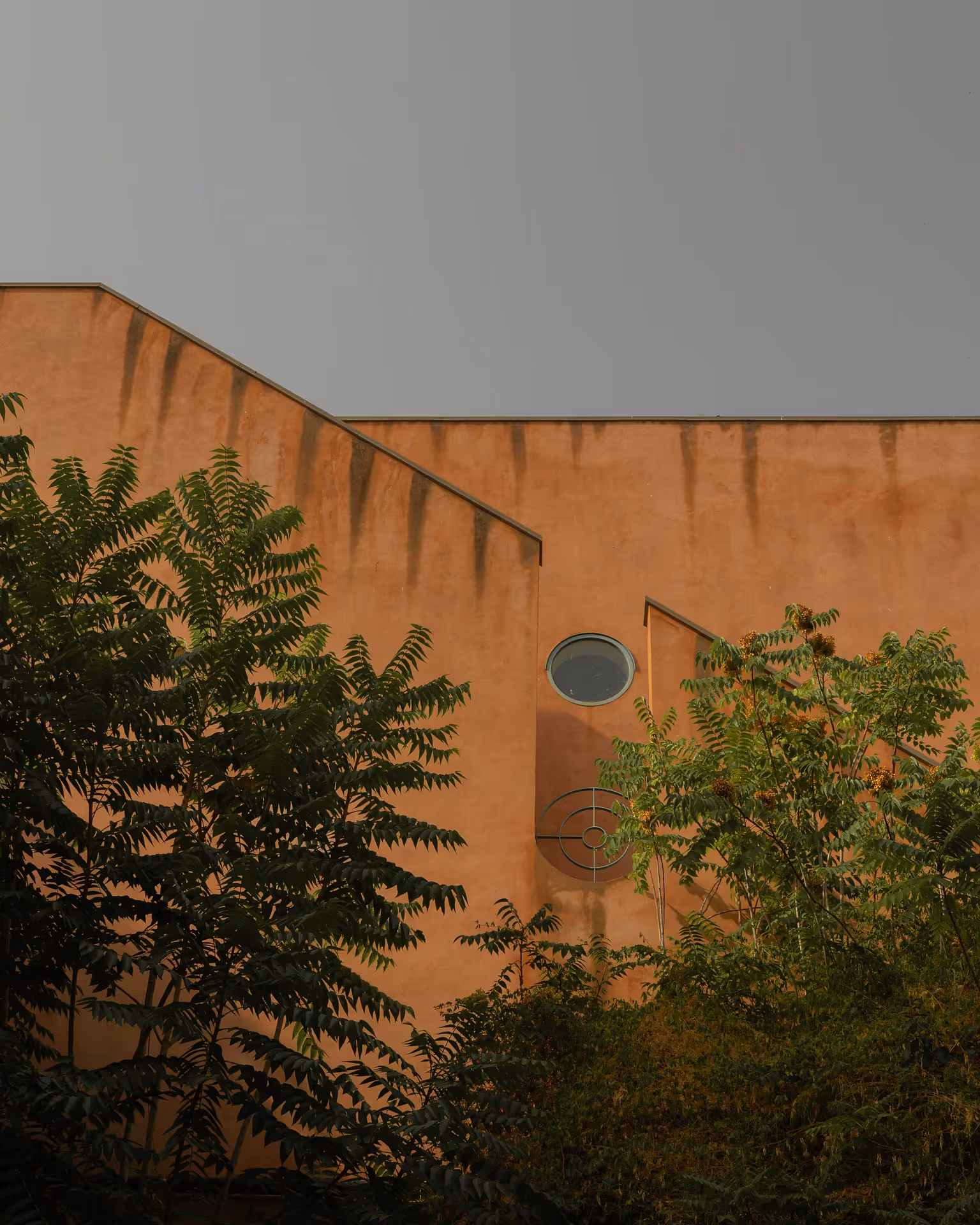 Weathered orange concrete wall with light green trees in the foreground